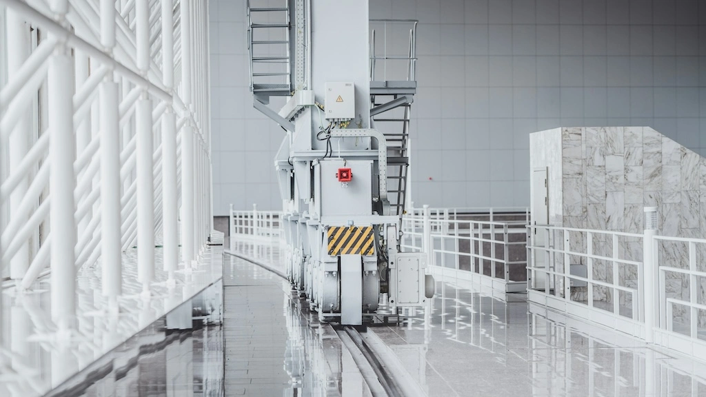 A bright picture of a moveable staircase in a clean factory, with a fence on one side and pillars on the other.