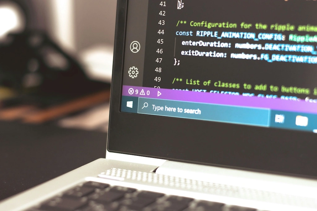 Closeup of a corner of a laptop screen. The screen shows the windows taskbar and the program Visual Studio Code, with some code.