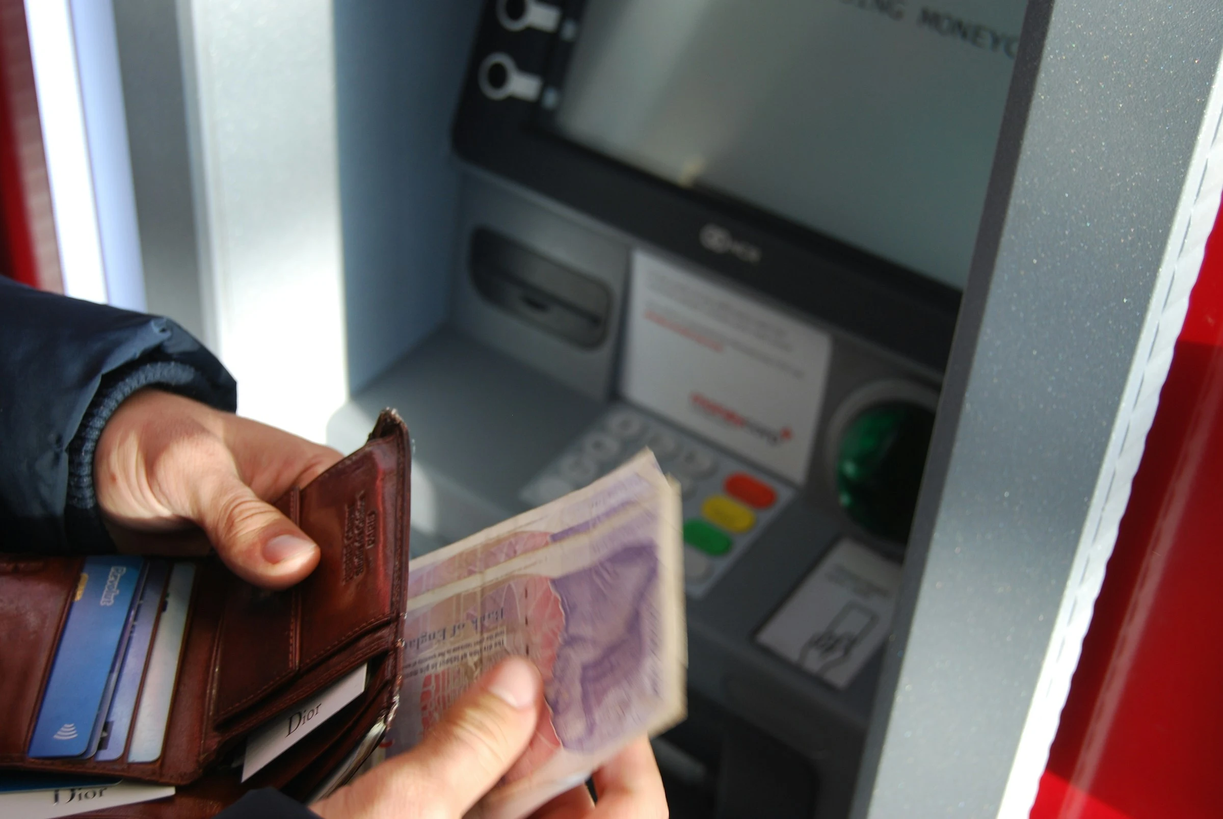 A closeup of a person standing in front of an ATM, putting money into their wallet. Only their hands are in frame.
